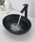 Oval dark vessel sink with black faucet and drain installed, water flowing into basin, modern design, ceramic, on marble counter