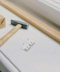 Stainless Steel Fridge Shelf Support Clips 8 Pack With Brushed Finish next to a hammer and wooden plank on a white surface