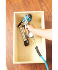 Rock Solid 18 Gauge Brad Nailer with Slick Trigger and Compact Narrow Nose for Tight Corners, held with a hose in a wooden box.