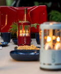 Red Candle Lantern For Camping And Emergencies on picnic table with food, showing aluminum body and glass chimney.