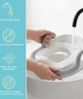 Hands holding a gray and white Toddler Potty Training Seat And Step Stool Two In One Frame with water running over it for cleaning.
