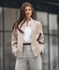 Fashionable woman in beige coat and white shirt standing in urban setting
