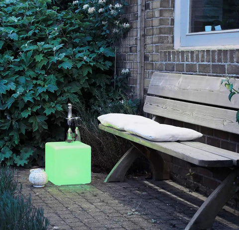 Rechargeable 12 Inch LED Light Cube Stool With Remote Control Mood Lamp in patio beside a wooden bench with greenery background