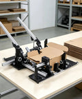 Universal Adjustable Manual Box Folding Tool With Slick Slider For No Sweat Cardboard Sealing And Smooth Shipping Operations A Solid Game Changer At Sixty Five Centimeters Long on a tabletop with folded cardboard.