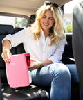 Woman using Dope Portable 4L Mini Fridge And Cooler Warmer For Bedroom, Car, Desk And Dorm Room, 6 Can Capacity, USB Power, 12V AC DC Ready, Pink Finish For Food, Drinks, Skincare And Makeup On The Go in the backseat of a car.