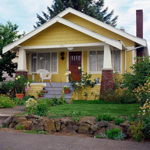 Yellow house with porch featuring decorative porch ceiling light and garden view.