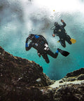 Two divers using Donut Wing For Technical Scuba Diving With Inflator Hose And K Style BPI 40 Lbs 18 Kg Capacity Black Ultra Durable 1000D Cordura Outer Shell And 500D Inner Bladder Eco Friendly Dope Dyed Fabric For Abrasion Resistance underwater near rocks