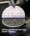 Gloved hand holding Trizact Hookit 3 Inch P1000 Grit Blending Disc Gray, showing hook and loop system for auto body sanding.